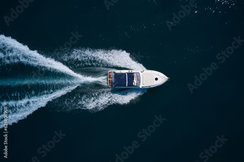 Wallpaper Mural A large white boat with a blue awning is moving fast on dark water. Top view. Big white motor yacht movement on dark water top view. Torontodigital.ca