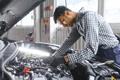 Indian car mechanic standing and working in service station. Car specialists examining the lifted car. Professional repairmen wearing mechanic uniform in blue color.