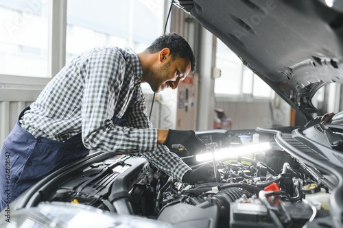 latin hispanic auto mechanic in uniform is examining a car while working in auto service