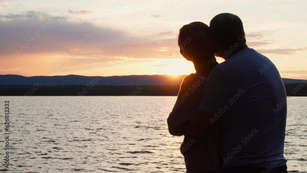 A couple in love stands on the shore of the lake at sunset and admires nature. Romantic relationships and harmony with nature.