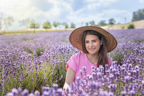 Closeup portrait of beautiful brunette smiling girl in straw hat and pink dress posing in purple lavender field.  Horizontally. 