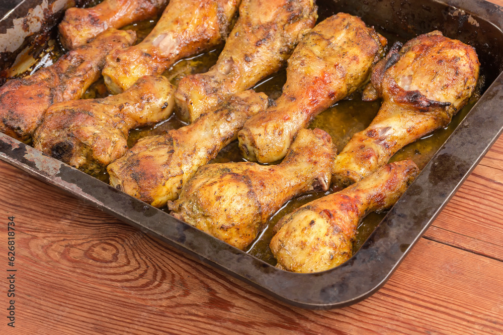 Baked chicken legs on metal oven-tray on rustic table