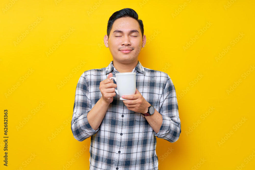 Handsome young Asian man wearing a white checkered shirt enjoying a cup of coffee isolated on yellow background. People Lifestyle Concept Handsome young Asian man wearing a white checkered shirt enjoying a cup of coffee isolated on yellow background. People Lifestyle Concept