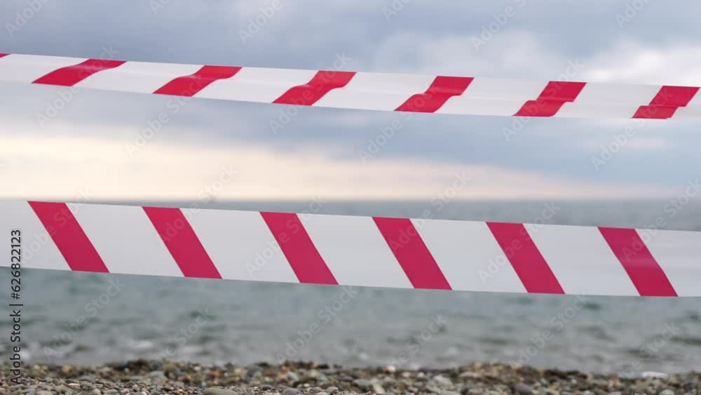 Red white warning tape barrier ribbon swinging in the wind across exotic sea beach background without people. No entry Red White caution tape. No holiday concept, delayed travel, no summer plans Red white warning tape barrier ribbon swinging in the wind across exotic sea beach background without people. No entry Red White caution tape. No holiday concept, delayed travel, no summer plans