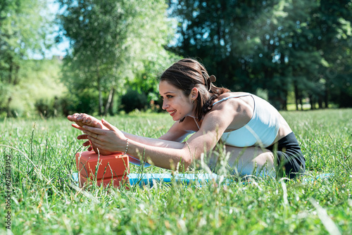 Female fitness trainer doing morning yoga exercises in green grass at park. Summer time for sport