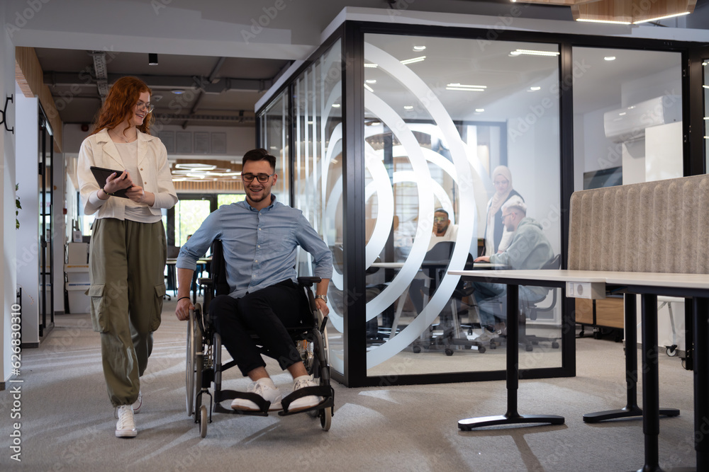Young business colleagues, collaborative business colleagues, including a person in a wheelchair, walk past a modern glass office corridor, illustrating diversity, teamwork and empowerment in the Young business colleagues, collaborative business colleagues, including a person in a wheelchair, walk past a modern glass office corridor, illustrating diversity, teamwork and empowerment in the