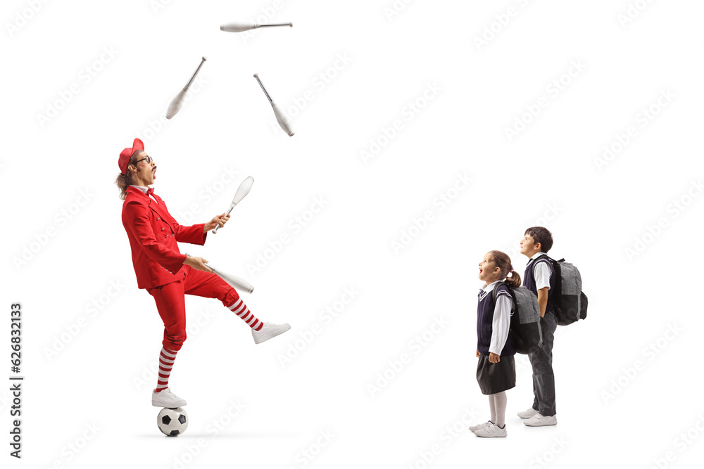 Children watching a man in a red suit standing on a ball and juggling