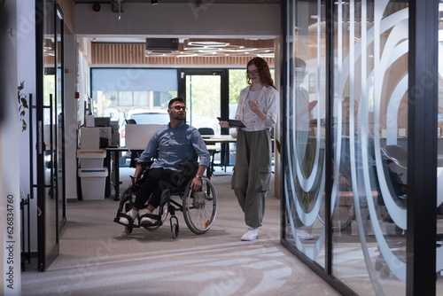 Young business colleagues, collaborative business colleagues, including a person in a wheelchair, walk past a modern glass office corridor, illustrating diversity, teamwork and empowerment in the