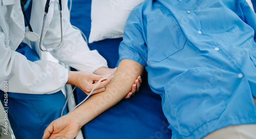 Female senior doctor holding male patient hand on the bed with receiving saline solution in hospital .