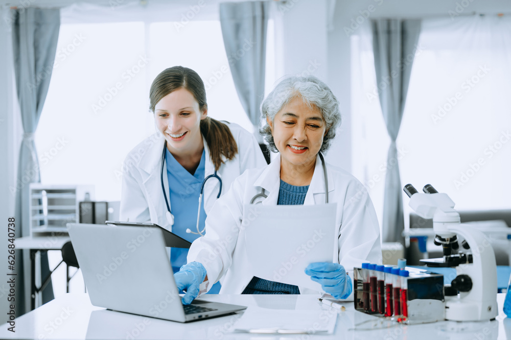 Medical team having a meeting with doctors in white lab coats and surgical scrubs seated at a table discussing a patients working online using computers in the medical industry..