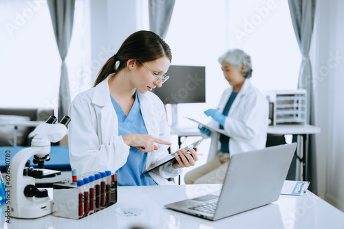 Two scientist or medical technician working  having a medical discuss meeting with an Asian senior female scientist supervisor in the laboratory with online reading  test samples and innovation