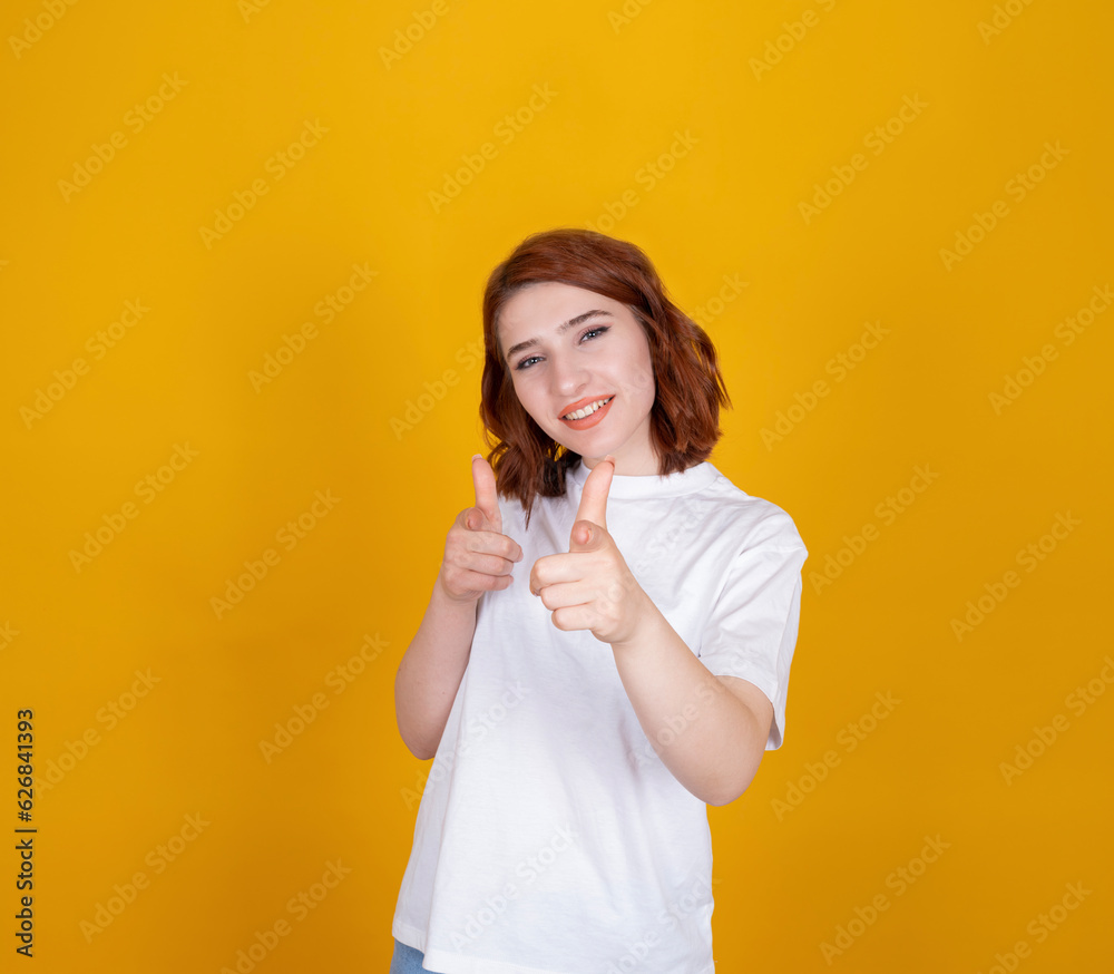 Pointing fingers to camera, young beautiful red hair girl pointing fingers to camera. Caucasian lady wearing casual white shirt. Isolated orange yellow background. Happy funny smiling positive face. Pointing fingers to camera, young beautiful red hair girl pointing fingers to camera. Caucasian lady wearing casual white shirt. Isolated orange yellow background. Happy funny smiling positive face.