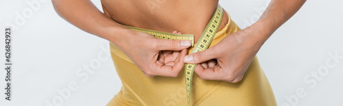 weight loss, cropped view of woman measuring waist with tape on white background, body size, banner