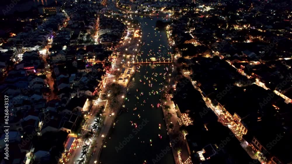 Vue aérienne de la l'ancienne ville de Hoian au Vietnam de nuit.  On y voit les bateaux illuminés par des lanterne sur la rivière. Cette ville est inscrite au patrimoine mondiale de l'Unesco.