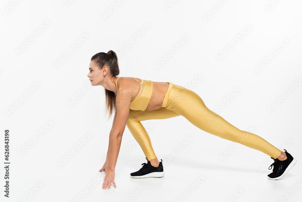 fit sportswoman in sneakers training and looking away on white background, physical activity concept