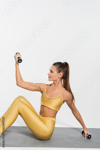 Fototapeta Naklejka Na Ścianę i Meble -  sportswoman in yellow active wear working out, dumbbells, fitness mat, white background