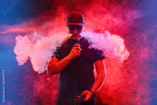Man engaged in vaping. Adult vaper guy on neon background. Vaper man releases steam from nose. Vape shop concept. Enjoy vaper smoking. Buying e-cigs in vape shop. Electronic cigarettes.