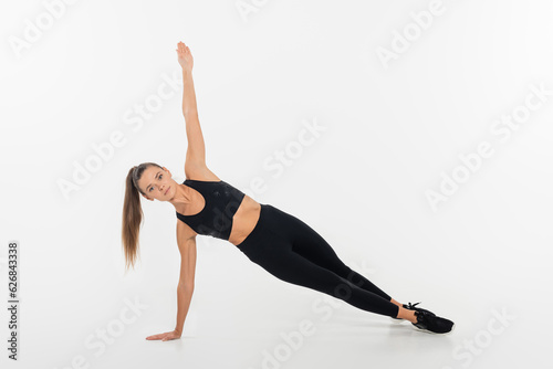 woman in fitness clothes doing side plank on white background, healthy and fit concept © LIGHTFIELD STUDIOS
