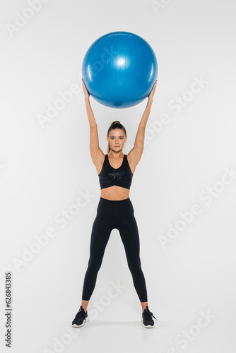 sportswoman holding stability ball and looking at camera while training on white background