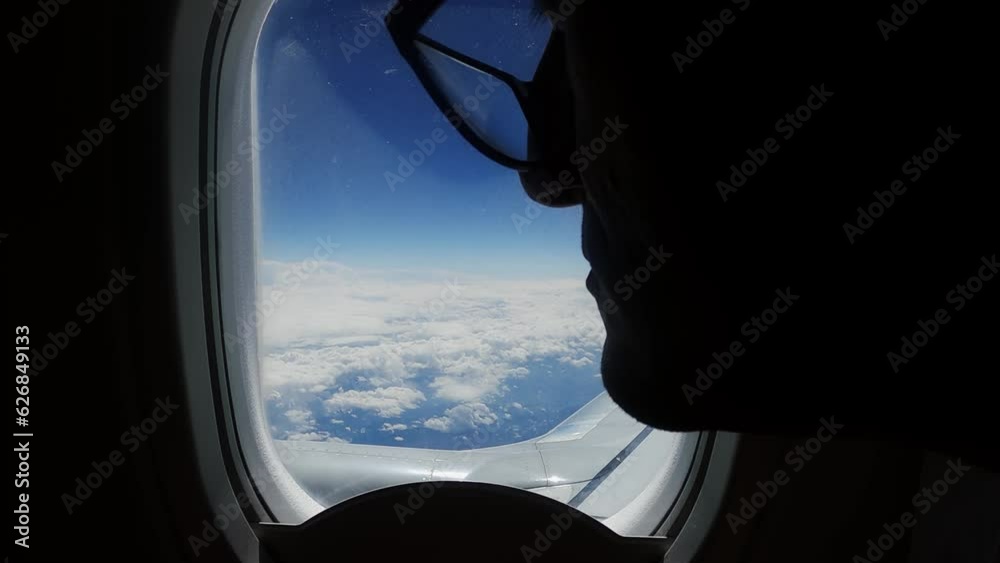 Nostalgic sad man look on plane wing through window on flight over clouds against blue sky