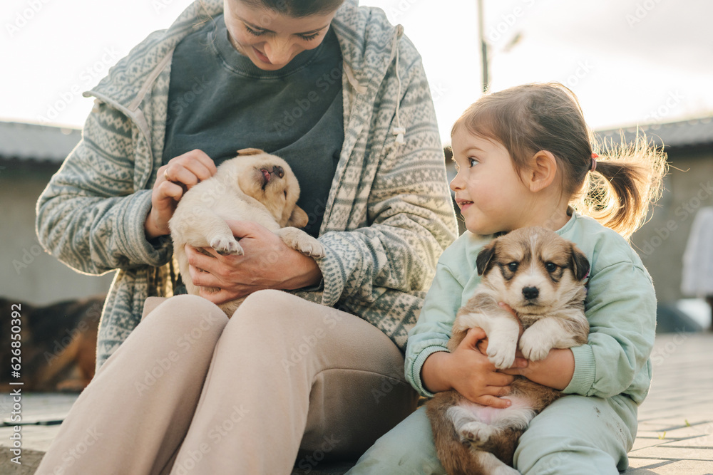 Mother and cute daughter playing with adorable puppies dog outdoors in the backyard. Lifestyle concept. Happy family concept. Happy family day. Mother nature.