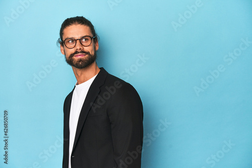 Businessman in suit with eyeglasses and beard looks aside smiling, cheerful and pleasant.