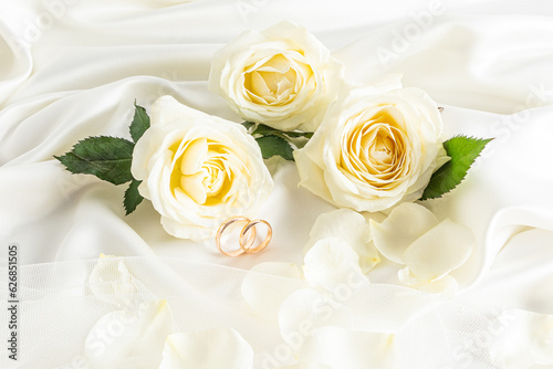 A beautiful wedding arrangement with a pair of wedding gold rings on a beige satin background and three tea roses. Layout for invitations, postcards.