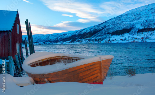 Beautiful winter landscape with old fishing red cabin (boathouse) boat at sunset - Red wooden boathouse and boat covered with layers of snow - Tromso, Norway photo