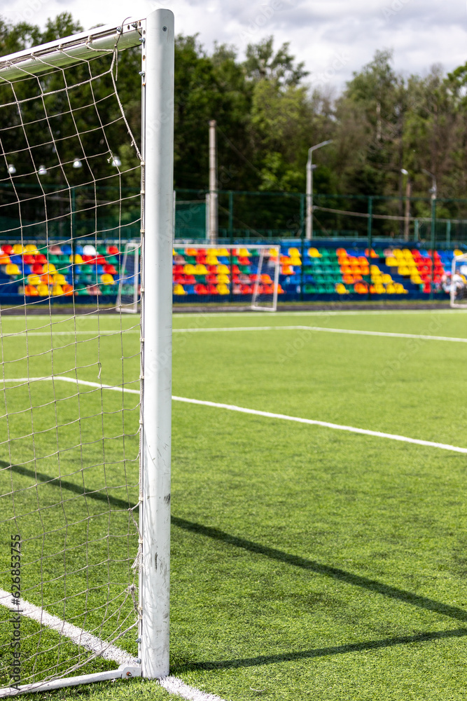 Fototapeta premium Artificial turf on the football field. Part of the football goal and green synthetic grass on the sports field on the background of colorful seats.