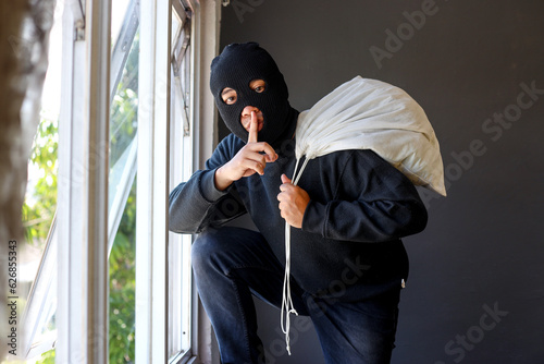 фотографія Thief in black clothes wearing a mask carrying a large bag of loot over his shou