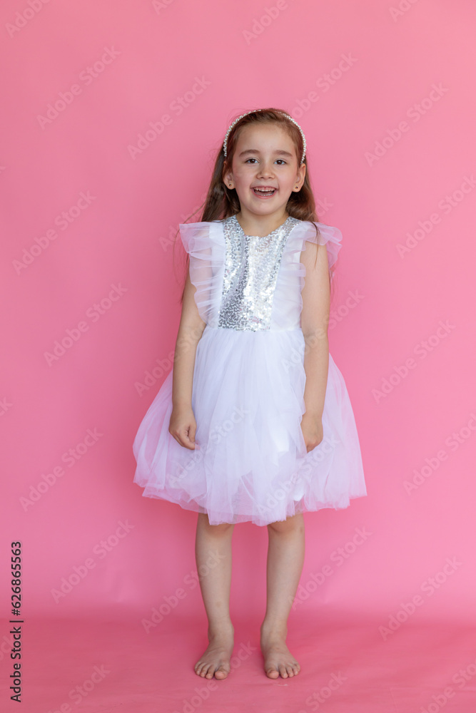 Cute happy laughing little girl in a pink princess dress posing on pink background. Kids Birthday party celebration concept. Happy Birthday banner with copy space. Studio shot. Cute happy laughing little girl in a pink princess dress posing on pink background. Kids Birthday party celebration concept. Happy Birthday banner with copy space. Studio shot.