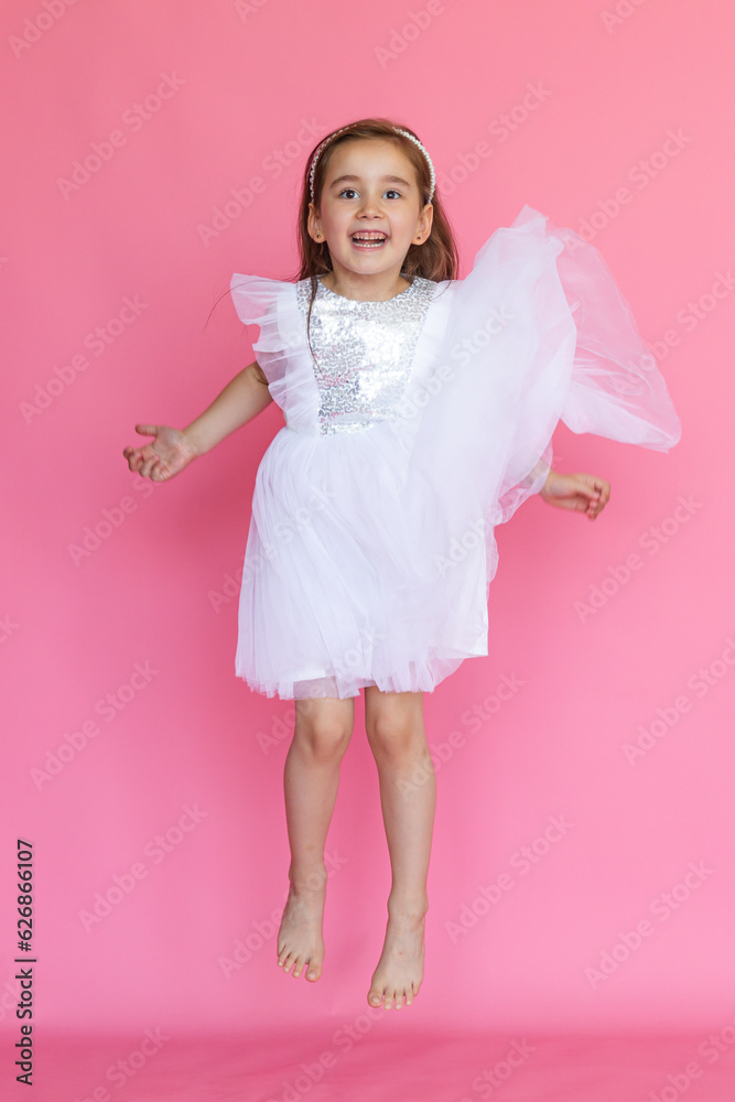 Cute happy little girl in a pink princess dress has fun and jumping on pink background. Kids Birthday party celebration concept. Happy Birthday banner with copy space. Studio shot.