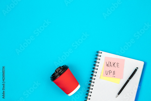 Paper cup and notebook with paper reminder with text Wake up, top view. photo