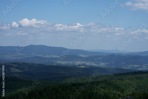 zdjęcie przedstawiające krajobraz górski wysokie szczyty i doliny nad którymi jest niebieskie niebo z kłębiącymi się chmurami. Lasy w dolinach gór, krajobraz górski natura i cisza i spokój