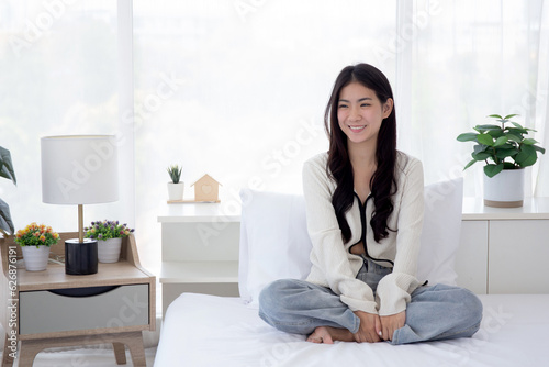 Happy beautiful young asian woman sitting on bed with cozy in the bedroom at home, portrait teenage cheerful smile with happiness and comfortable after awake, one person, lifestyles concept.