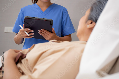 Nurse writing report document about medical and health care on tablet while explaining and check and diagnostic with elderly patient in hospital, examining disease, senior unwell while nurse visit.