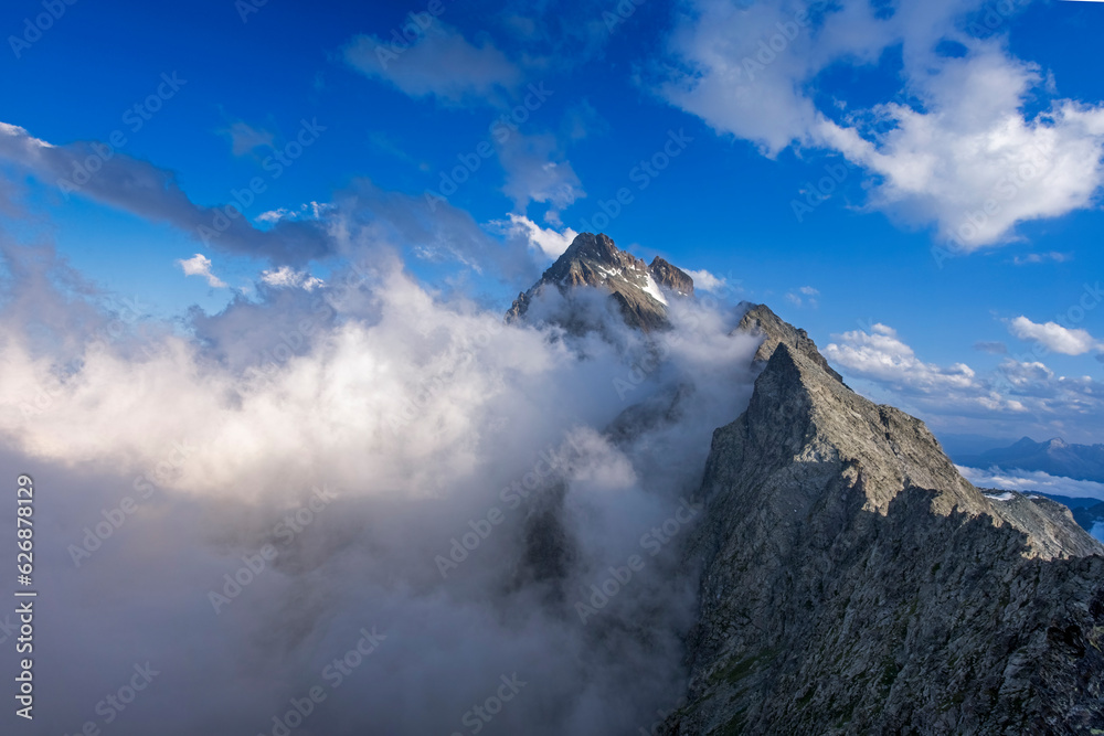Monte Viso or Monviso, the highest mountain in the Cottian Alps (3841 m). surrounded by clouds against blue sky taken on a summer evening from an observation point 3100 m above sea level. Piedmont.