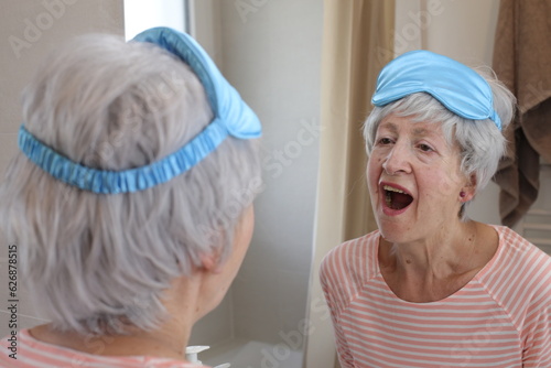 A sleepy looking senior woman in her sixties is staying in front of the mirror photo