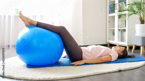 Beautiful young woman lying on fitness mat and training with blue fitball. Concept of healthcare, sports and yoga at home.