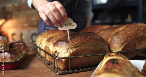 Sales Assistant In Bakery Putting Gluten Free Label Into Freshly Baked Baked Sourdough Loaves Of Bread