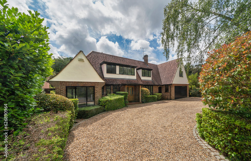 Luxury detached house in South East England with gravel drive and landscaped garden on summer day.