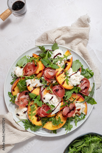 Healthy summer salad with peach, burrata, arugula and jamon