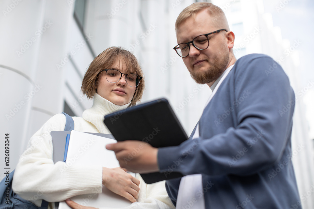 Back to university. The girl and the man are talking. A man shows something on tablet screen. Higher education. Students. Office workers. IT specialists Back to university. The girl and the man are talking. A man shows something on tablet screen. Higher education. Students. Office workers. IT specialists