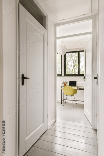 a hallway with white walls and wood flooring the door is open to an office area that has a yellow chair