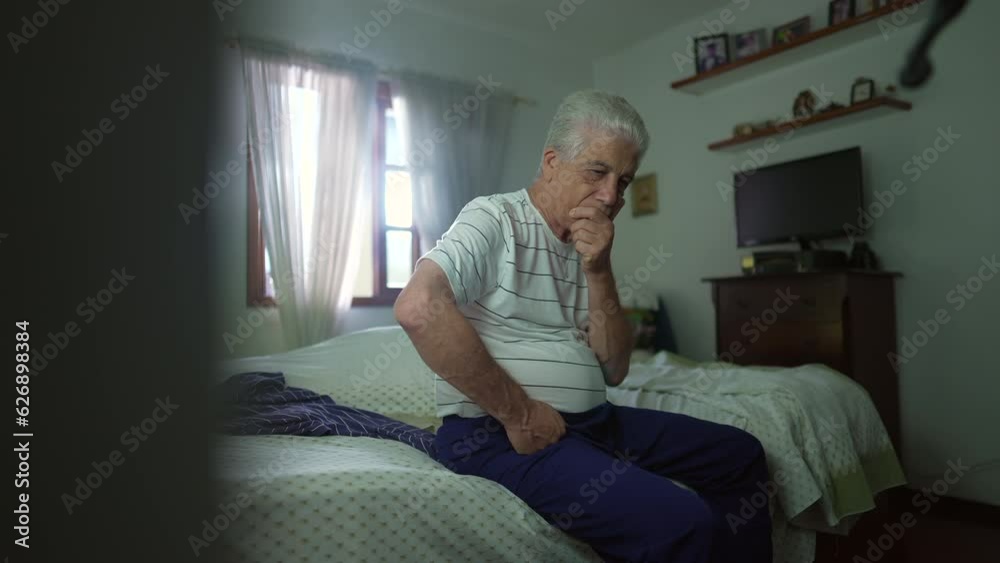 Pensive senior man seated by bedside in contemplation. Retired elderly person pondering decision with hand in chin in deep mental reflection in casual bedroom