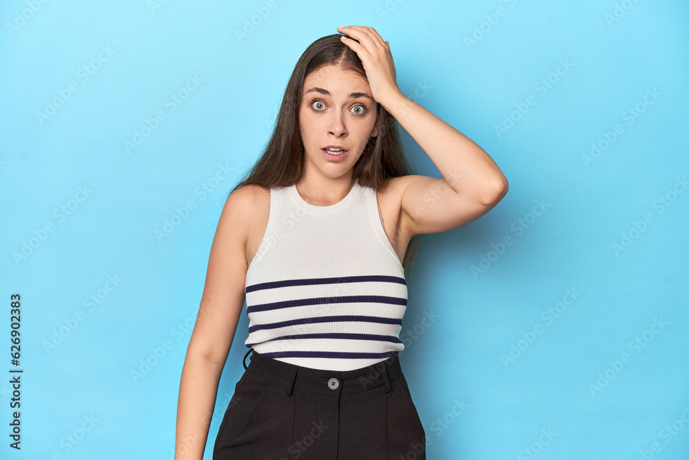 Woman in a striped top posing on a blue studio backdrop being shocked, she has remembered important meeting. Woman in a striped top posing on a blue studio backdrop being shocked, she has remembered important meeting.