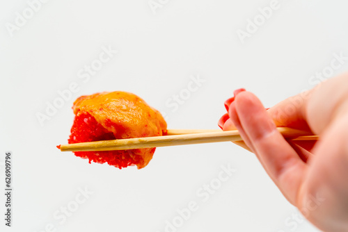 Close-up of baked sushi with shrimp and eel held with chopsticks by a man's hand on a white background