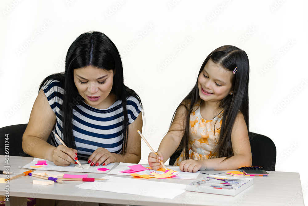 Young bunette woman and a little girl sitting at the desk and drawing together. Isolated on white. Young bunette woman and a little girl sitting at the desk and drawing together. Isolated on white.