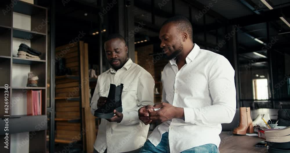 Two designer managers of a shoe factory are talking about a new batch of shoes. Two Black men in white shirts are discussing a new style of shoes in the office at their factory Two designer managers of a shoe factory are talking about a new batch of shoes. Two Black men in white shirts are discussing a new style of shoes in the office at their factory