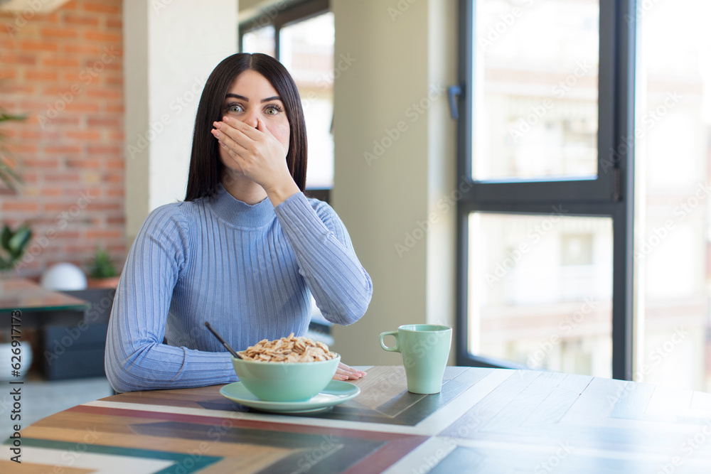 pretty young woman covering mouth with a hand and shocked or surprised expression. breakfast concept pretty young woman covering mouth with a hand and shocked or surprised expression. breakfast concept